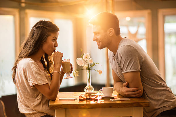 Ung kvinna dricker kaffe och kommunicerar med sin leende pojkvän på ett kafé.